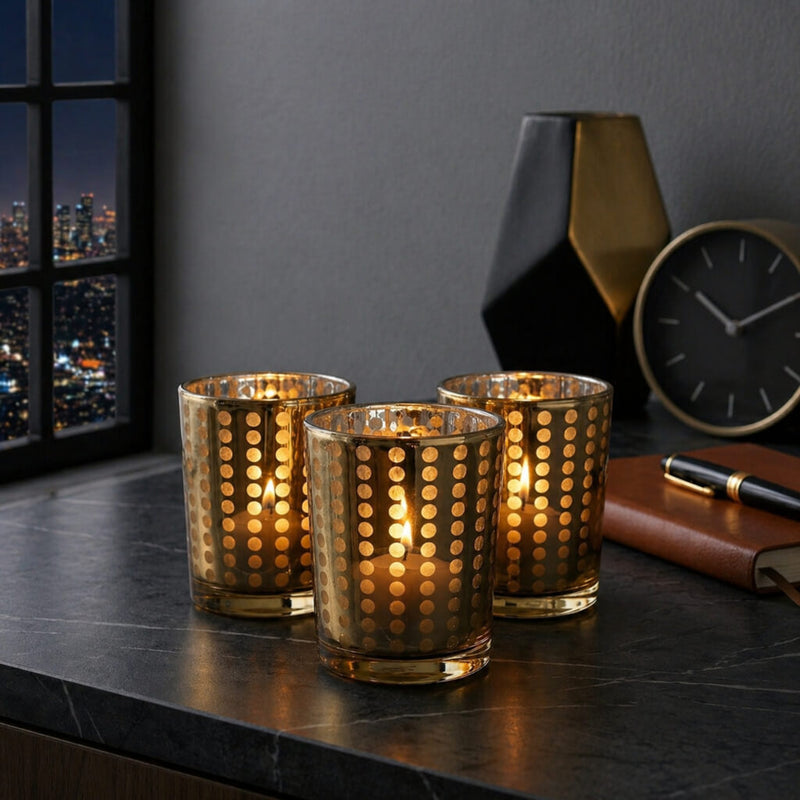 Three small gold dotted glass holders with glowing candles on a dark desk near a window - thumbnail number 8