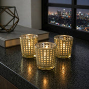 Three gold dotted votive holders lit on a granite counter with a city skyline in the background - thumbnail number 7