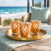 Lit candles in rose gold chevron candle holders on tray by oceanfront patio - thumbnail number 7