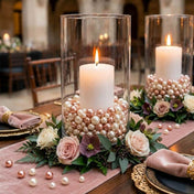 Lit white candles in glass cylinders filled with rose gold and off-white pearls on floral rings - thumbnail number 3