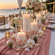 Lit white candles in glass cylinders filled with rose gold and off-white pearls at a beach wedding - thumbnail number 6