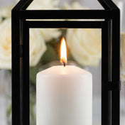 Close-up of a lit white pillar candle inside a black metal lantern with glass panels - thumbnail number 5