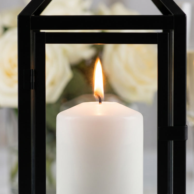 Close-up of a lit white pillar candle inside a black metal lantern with glass panels - thumbnail number 5