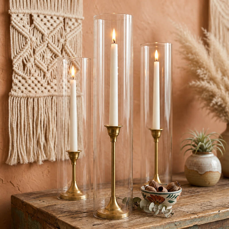 Lit white taper candles in gold holders with a chimney glass candle shade on a rustic wood table - thumbnail number 8