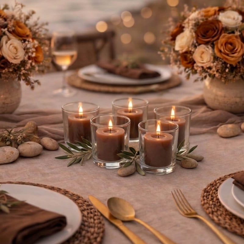 Five lit brown votive candles in glass holders on a table set with flowers and place settings - thumbnail number 5