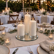 Lit pillar candles in glass cylinders on a mirror tray at an outdoor wedding table - thumbnail number 4