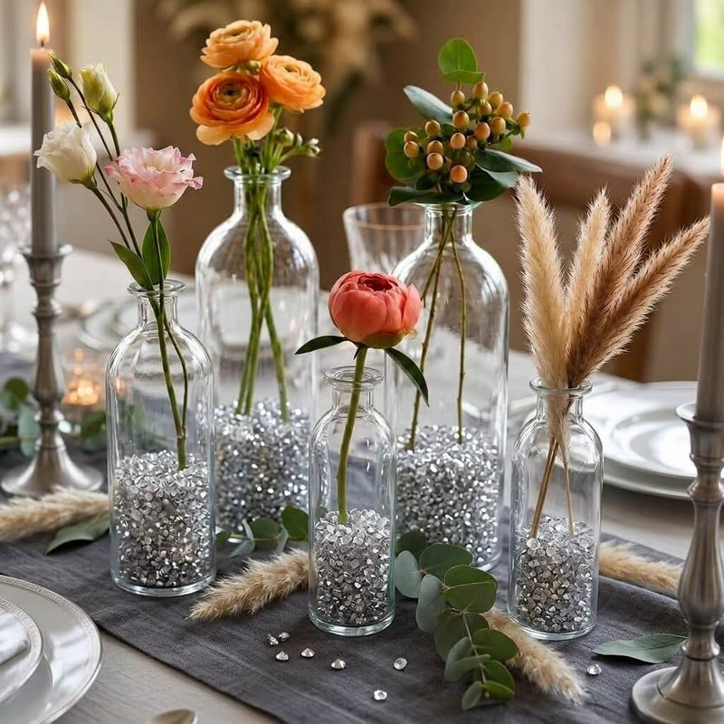 Fresh flowers in clear glass bottles filled with silver faux diamond gems on a dining table runner - thumbnail number 5