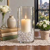Lit white pillar candle in a glass cylinder filled with clear acrylic ice beads on a table - thumbnail number 7