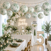 Green floral paper lanterns hang over a birthday setup with a lit number five - thumbnail number 4