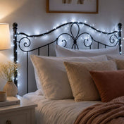 White LED fairy lights draped over a black metal scrollwork headboard in a bedroom - thumbnail number 8