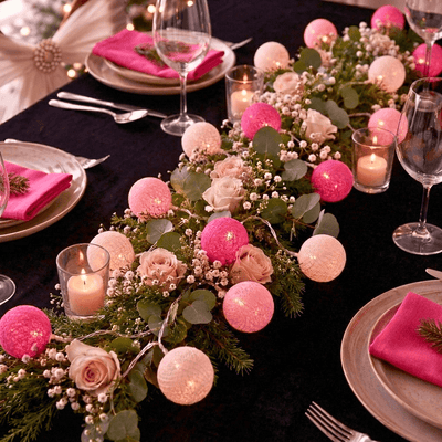 Pink and fuchsia cotton ball string lights decorate a holiday dinner table with roses and candles - thumbnail number 3