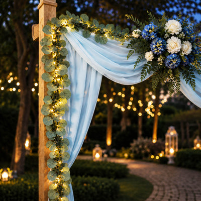 Eucalyptus garland lights frame a wedding arch draped with light blue fabric and blue and white flowers - thumbnail number 4