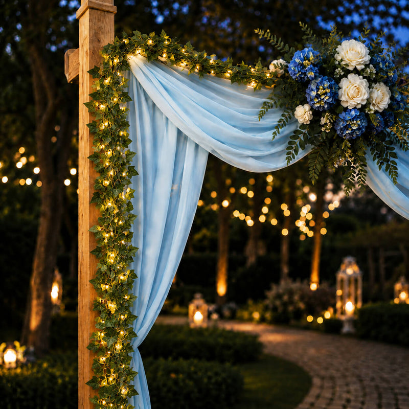 Ivy garland string lights wrap a wedding arch with light blue drapes and blue/white flowers - thumbnail number 4