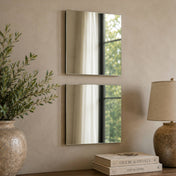 Two square mirrors mounted vertically on a light wall above a table with books and a lamp - thumbnail number 6