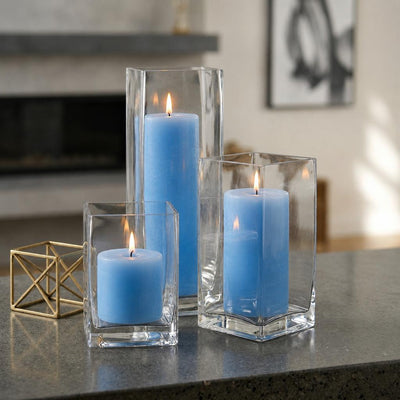 Three lit light blue candle and square holder sets clustered on a stone counter near a fireplace - thumbnail number 7