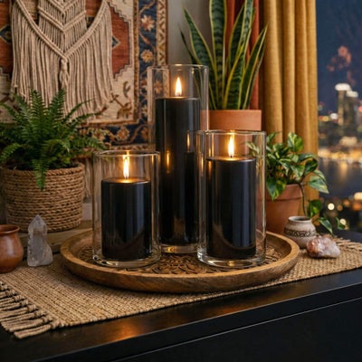 Lit black pillar candles in glass holders on a wooden tray surrounded by greenery - thumbnail number 3