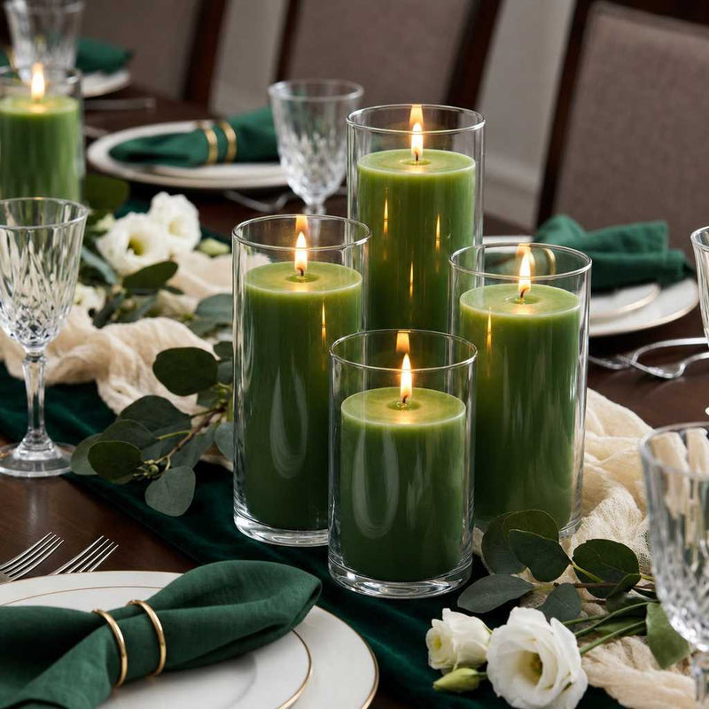 Four green pillar candles in glass cylinders on a table with a green runner and white flowers - thumbnail number 3