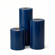 Three lit navy blue pillar candles in varied heights on a white background - thumbnail number 2