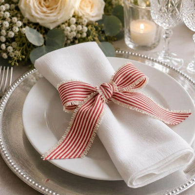 Red and white striped linen ribbon tied in a bow around a white napkin on a plate - thumbnail number 3