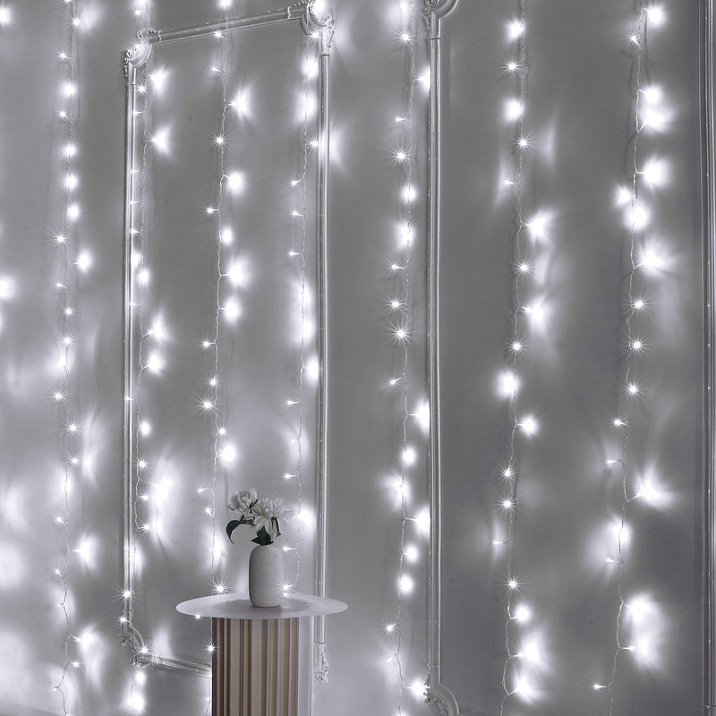 Cool white LED curtain lights hanging on a wall behind a small table with a floral vase. - thumbnail number 1