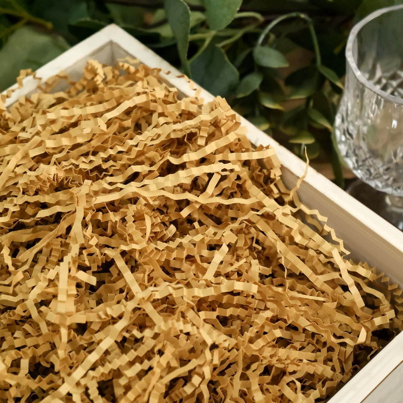 Shredded kraft paper filler in a wooden box with greenery and a glass nearby. - thumbnail number 1
